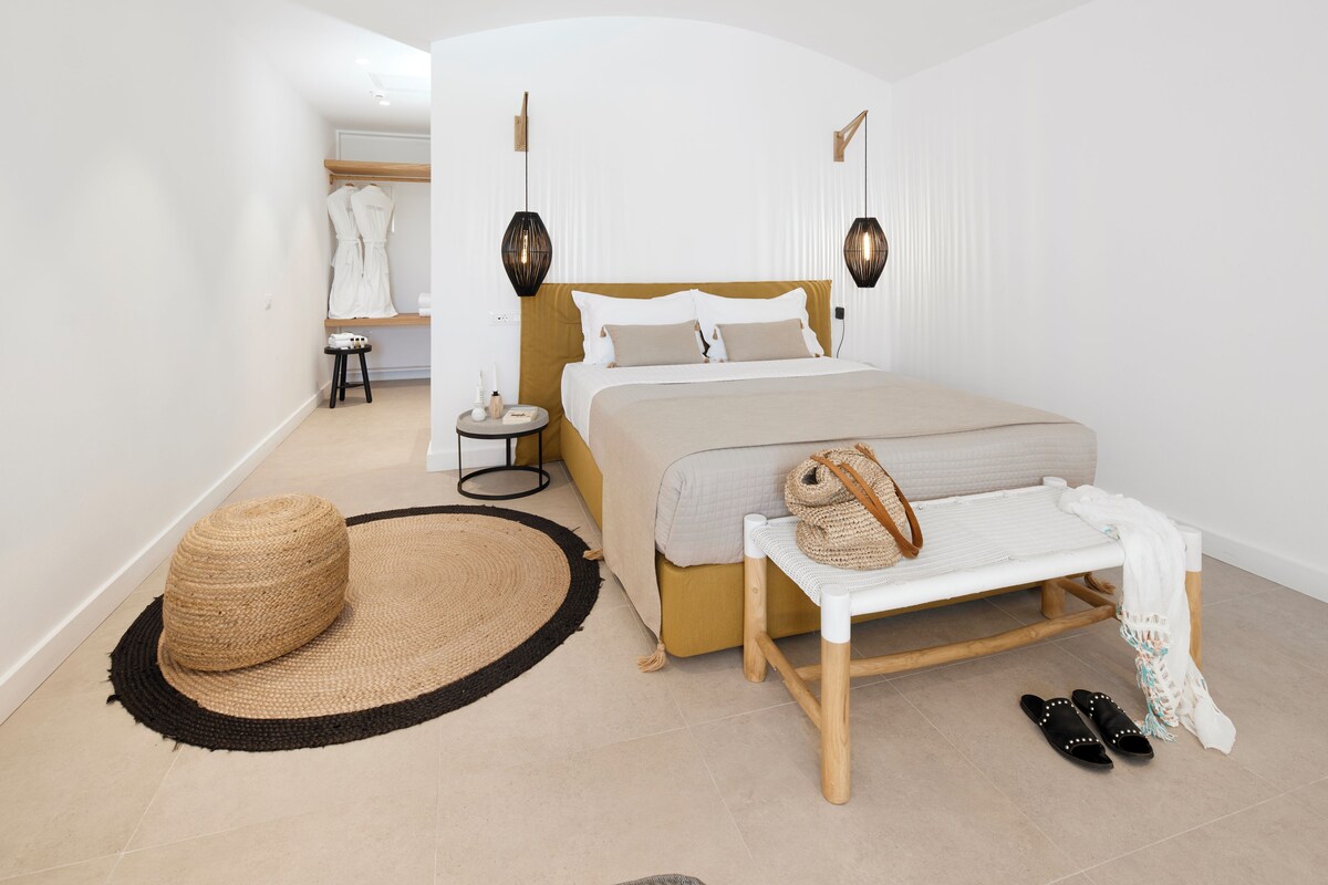 A modern bedroom with a large bed, bedside tables, a small stool, a woven basket, and a bench with shoes.