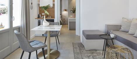 A modern living room with a dining area, a sofa, a coffee table, and a small kitchen in the background.
