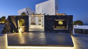 Edifici modern amb entrada de pedra, un rètol que diu "ALERA PARS Santorini Luxury Suites" i vista al mar.