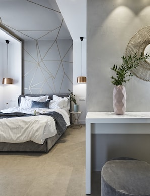 A modern bedroom with a geometric wall design, a bed with white and blue bedding, a small side table, a bedside lamp, and a decorative plant on a console table.