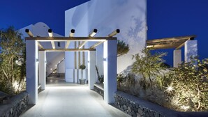Una estructura arquitectònica moderna amb una escala central que condueix a un nivell superior, envoltada de parets de pedra i plantes en testos.