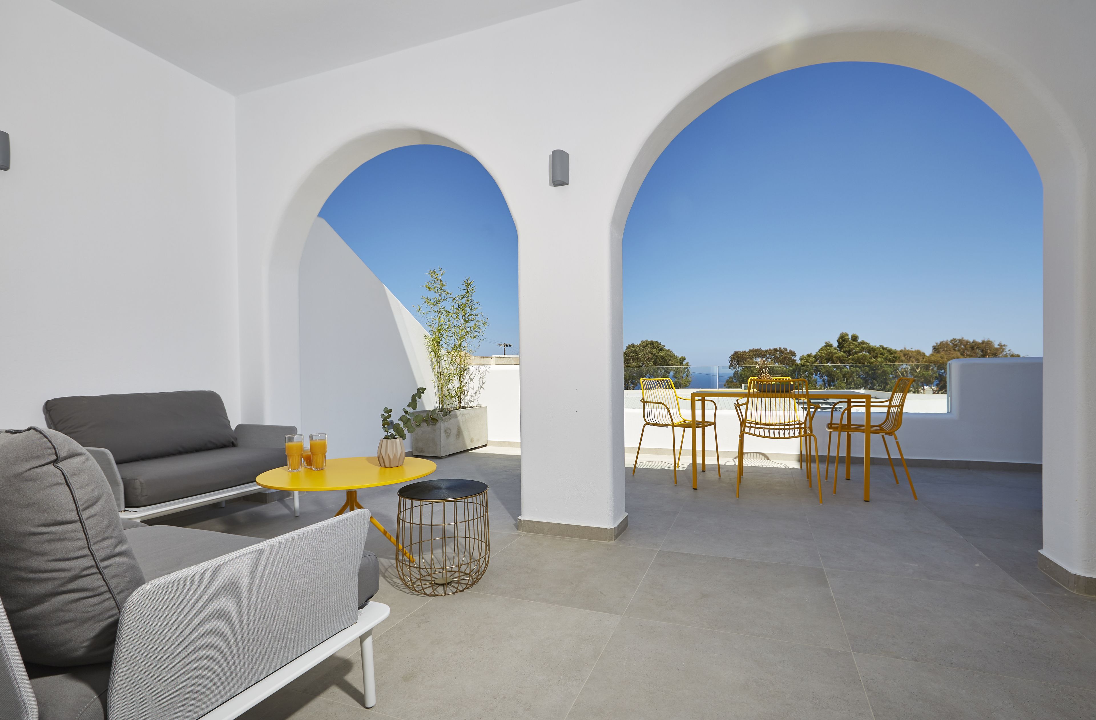 A modern outdoor seating area with a sofa, chairs, and a table, featuring a clear view of the sky and distant trees.