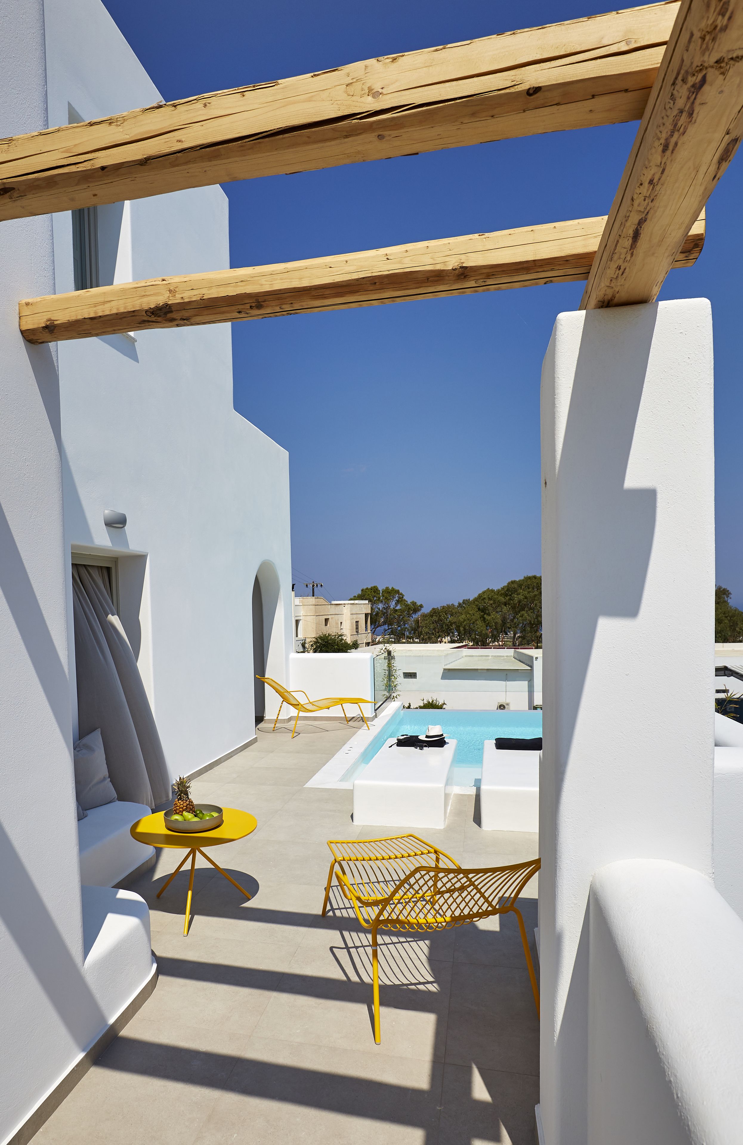 A modern outdoor patio with a pool, yellow chairs, and a small table with fruit.