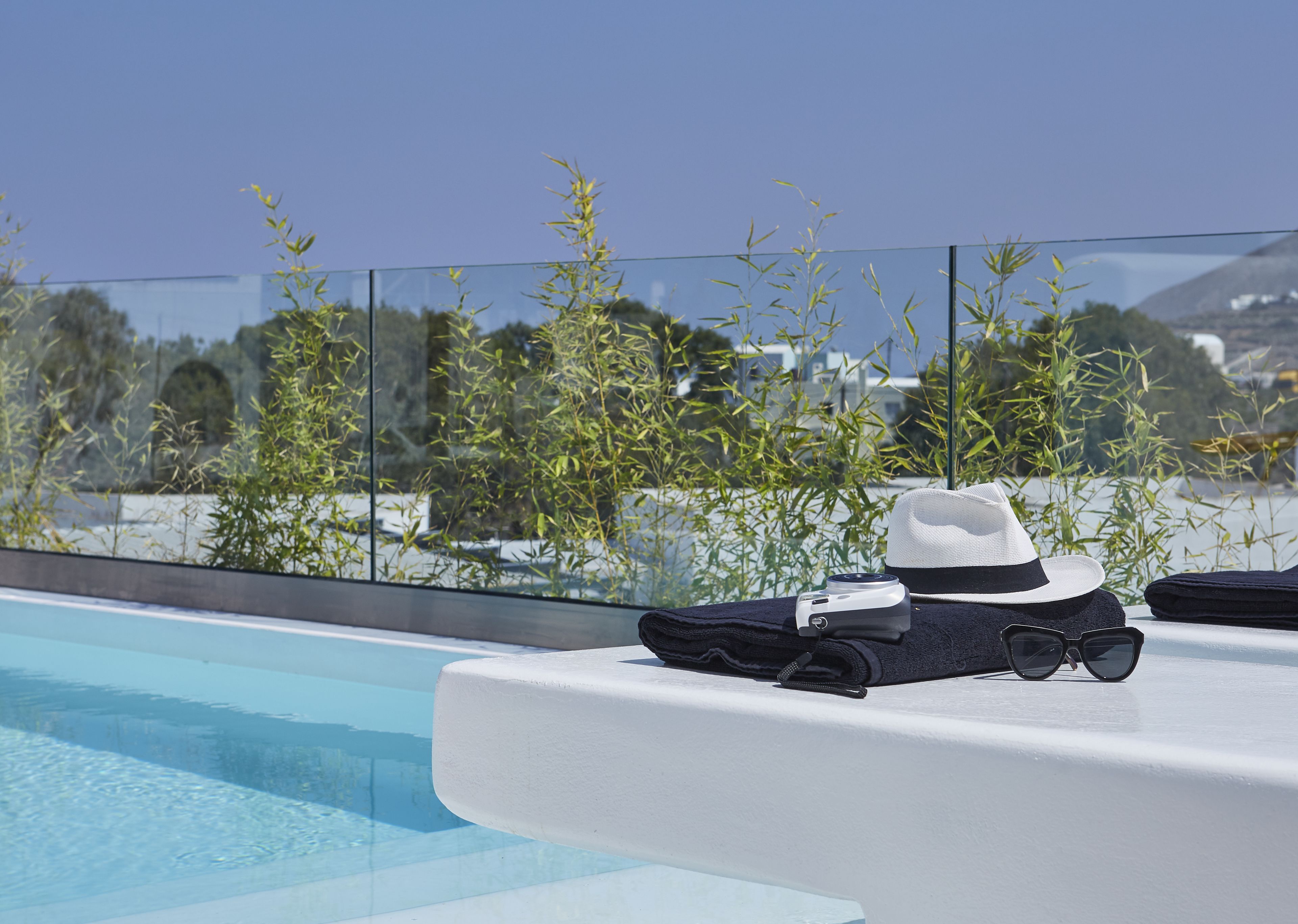 Ein Poolbereich mit einer weißen Liege, einem weißen Hut, Sonnenbrille und einer Kamera auf einer weißen Oberfläche.