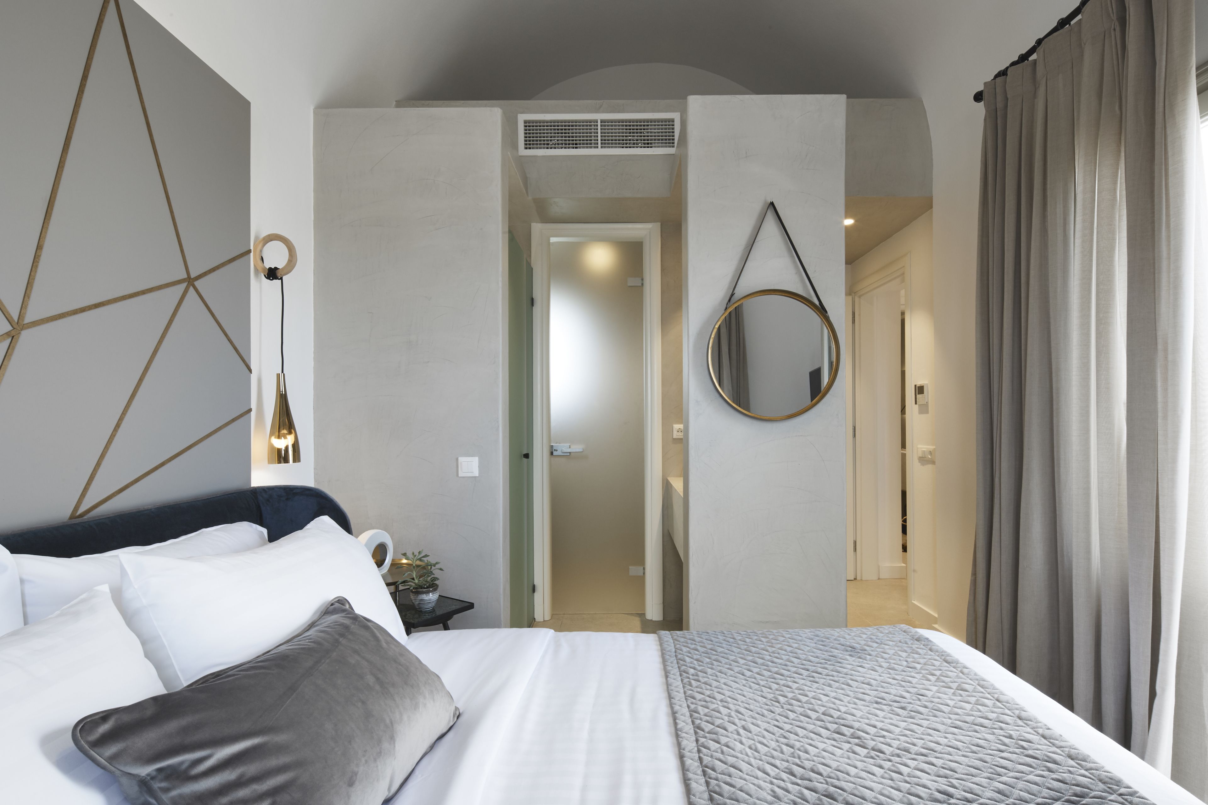 Une chambre à coucher moderne avec un grand lit, une table de chevet avec une lampe et un miroir au mur.