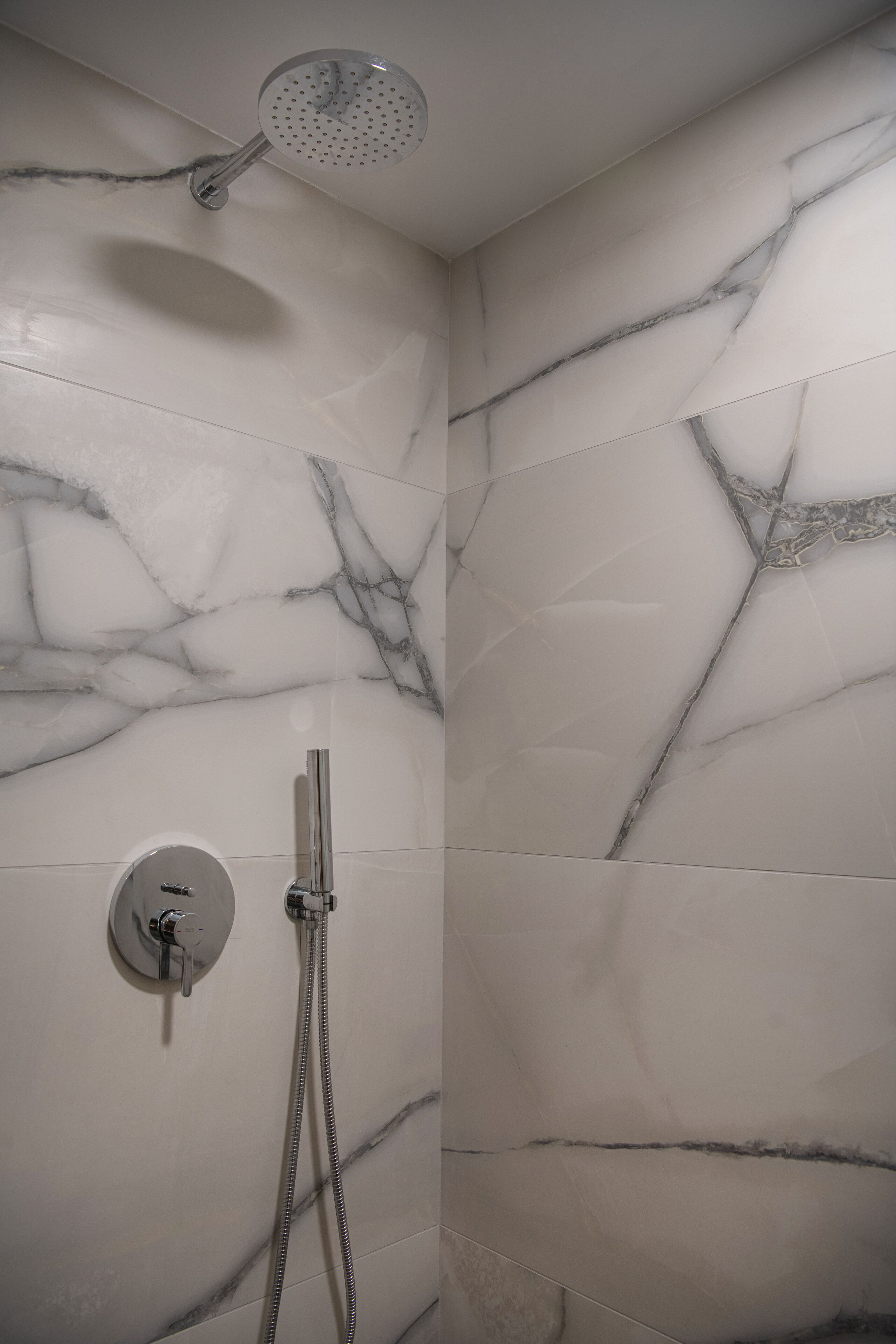 A shower with a handheld showerhead and a wall-mounted faucet.