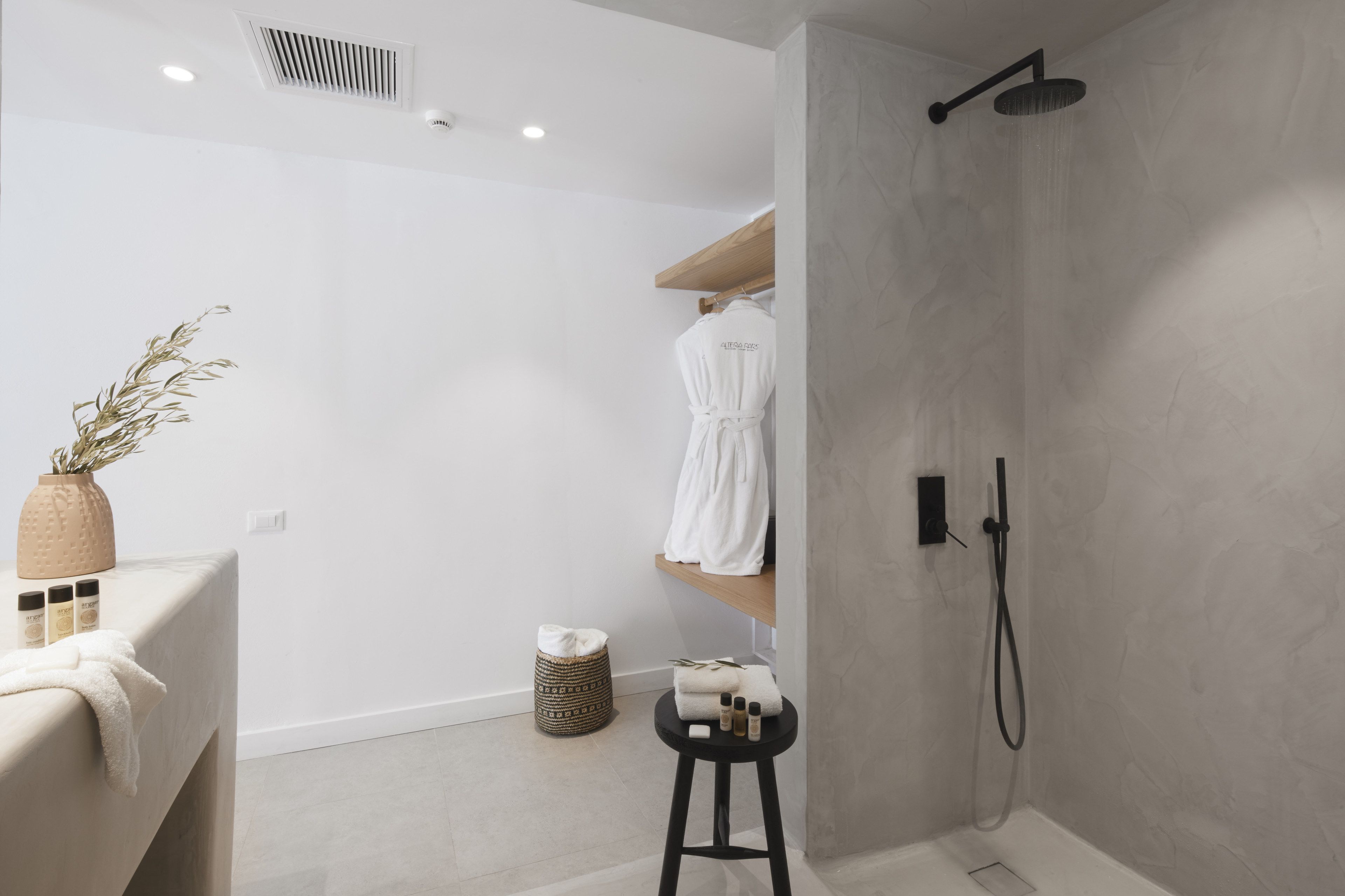 A modern bathroom with a shower, a towel rack, a small stool, and a shelf with toiletries.