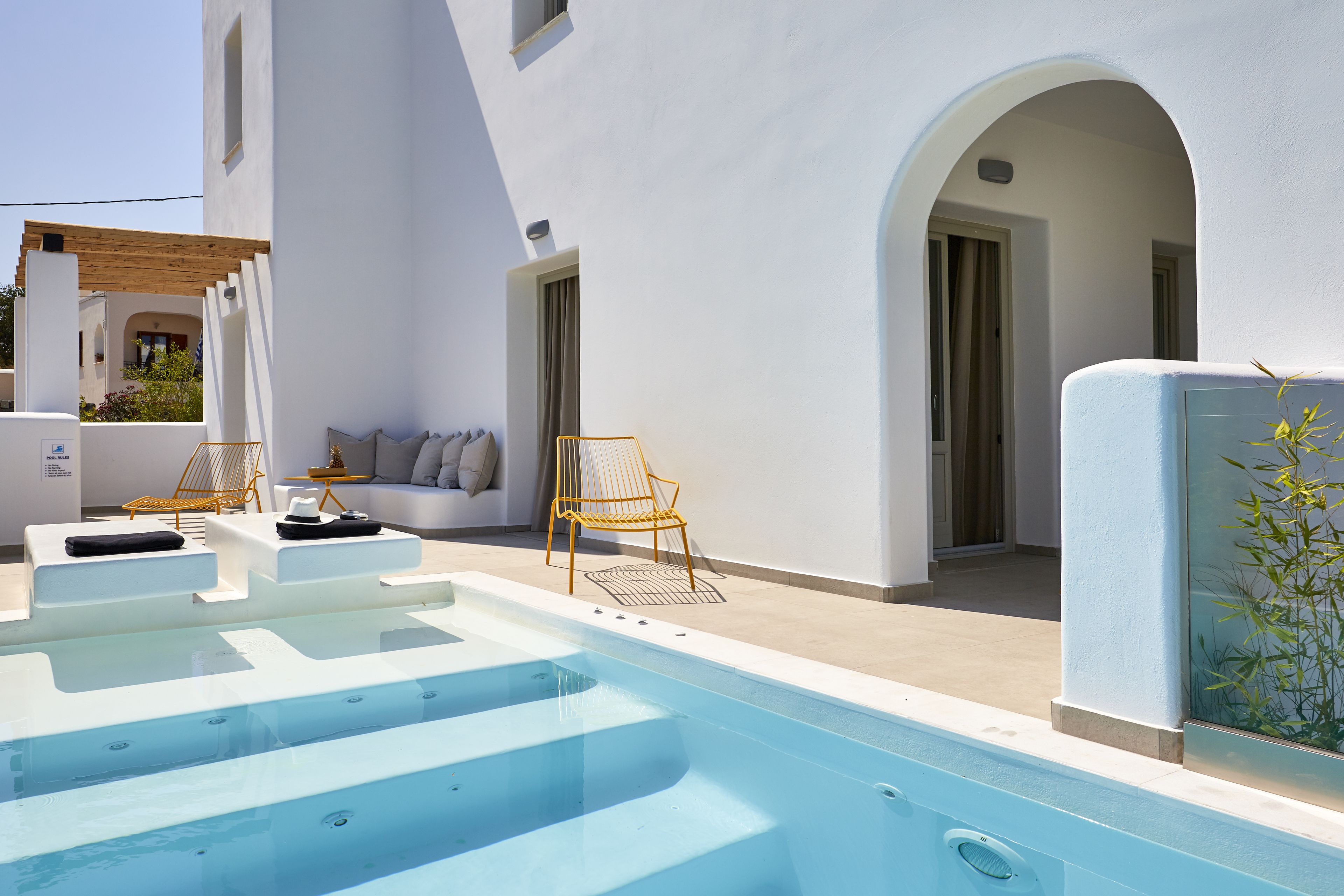 A modern outdoor pool area with a clear blue pool, white walls, and a wooden pergola.
