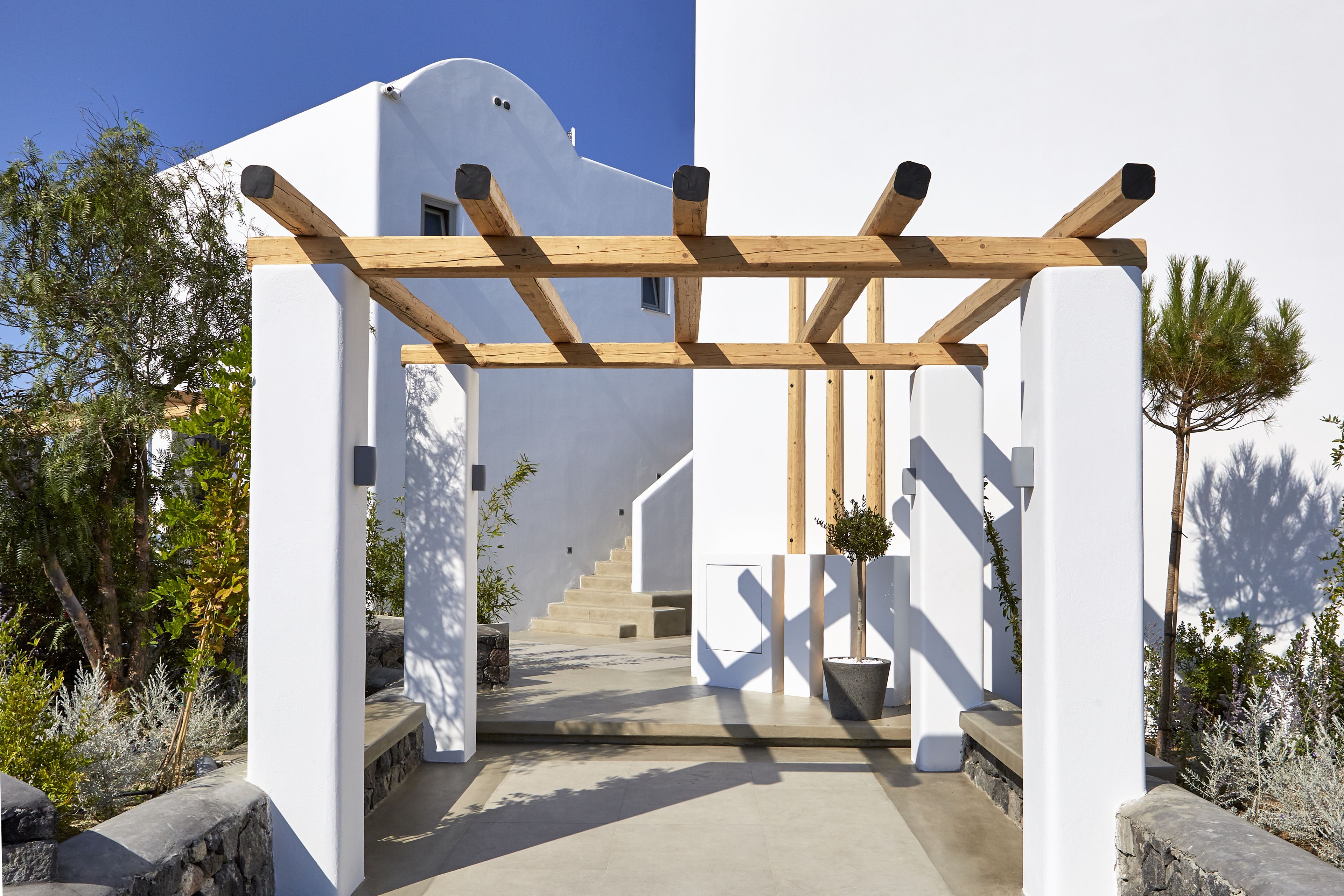 Un edificio moderno con fachada blanca, pérgola de madera y una escalera que conduce a la entrada.