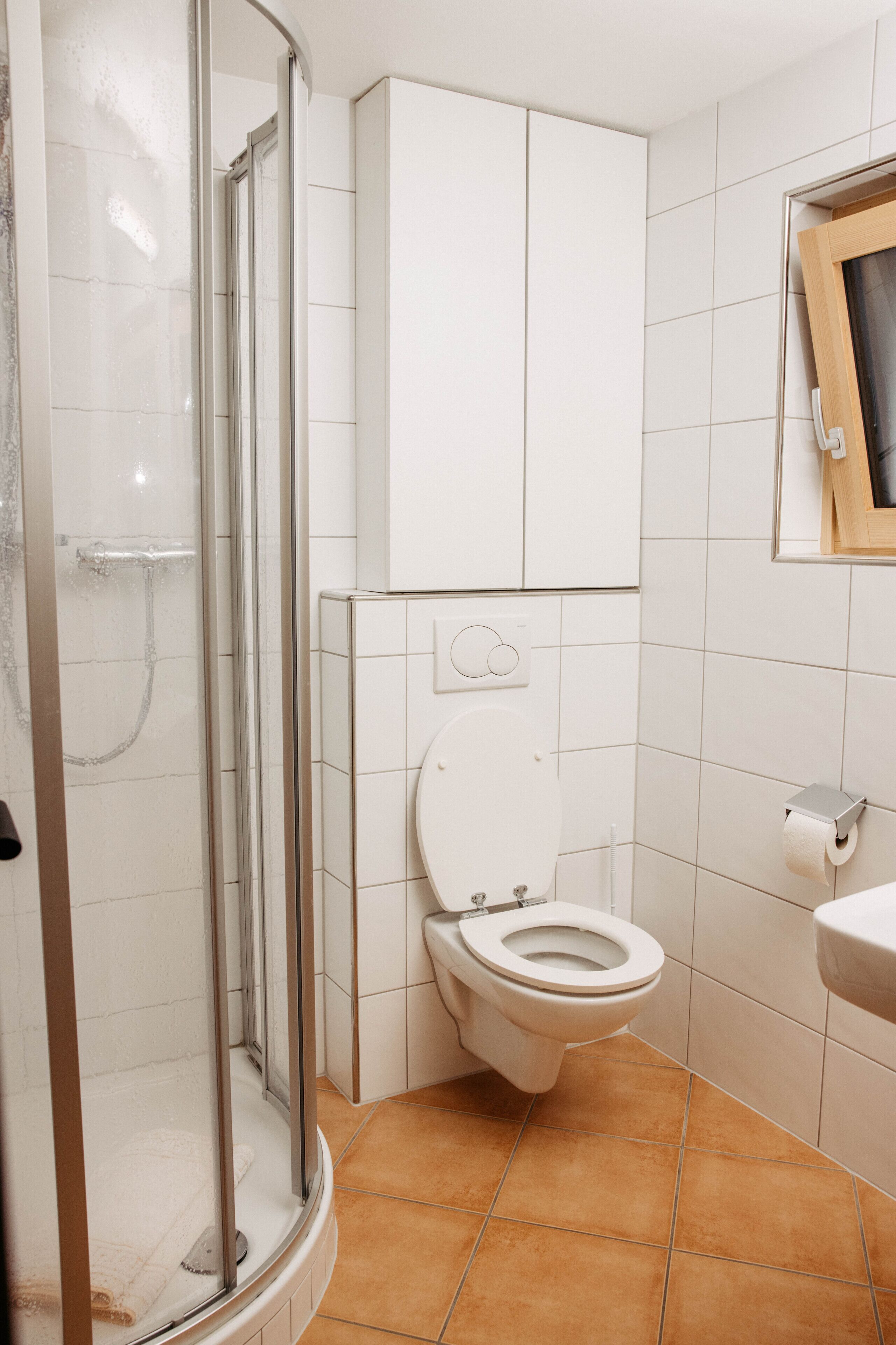 A bathroom with a glass shower enclosure, a toilet, and a sink.