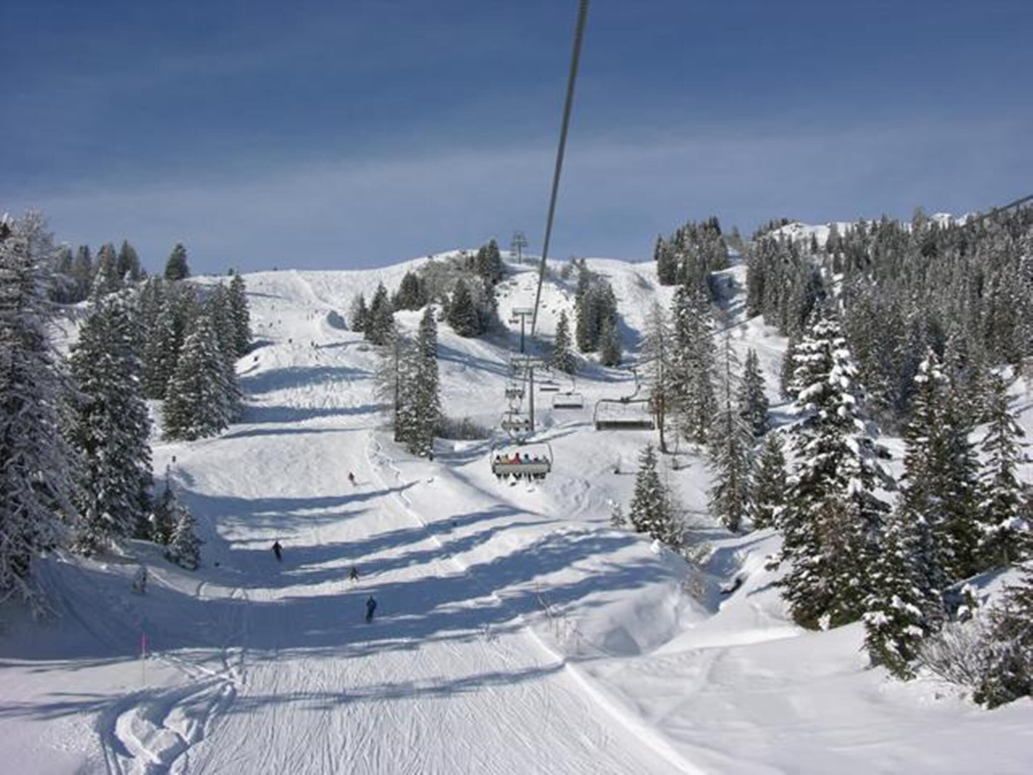 Une piste de ski avec un télésiège, des arbres et un paysage enneigé.