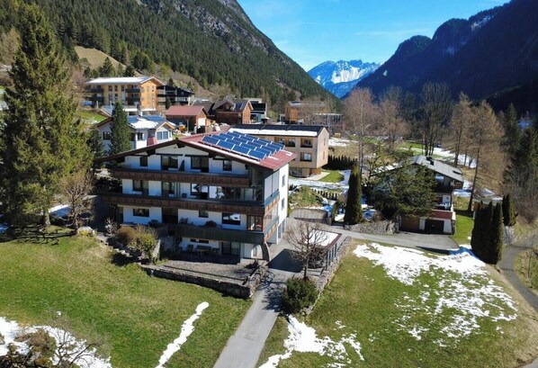A modern multi-story building with solar panels, surrounded by a mountainous landscape and a small parking area. - Kella-Egg (Brand)