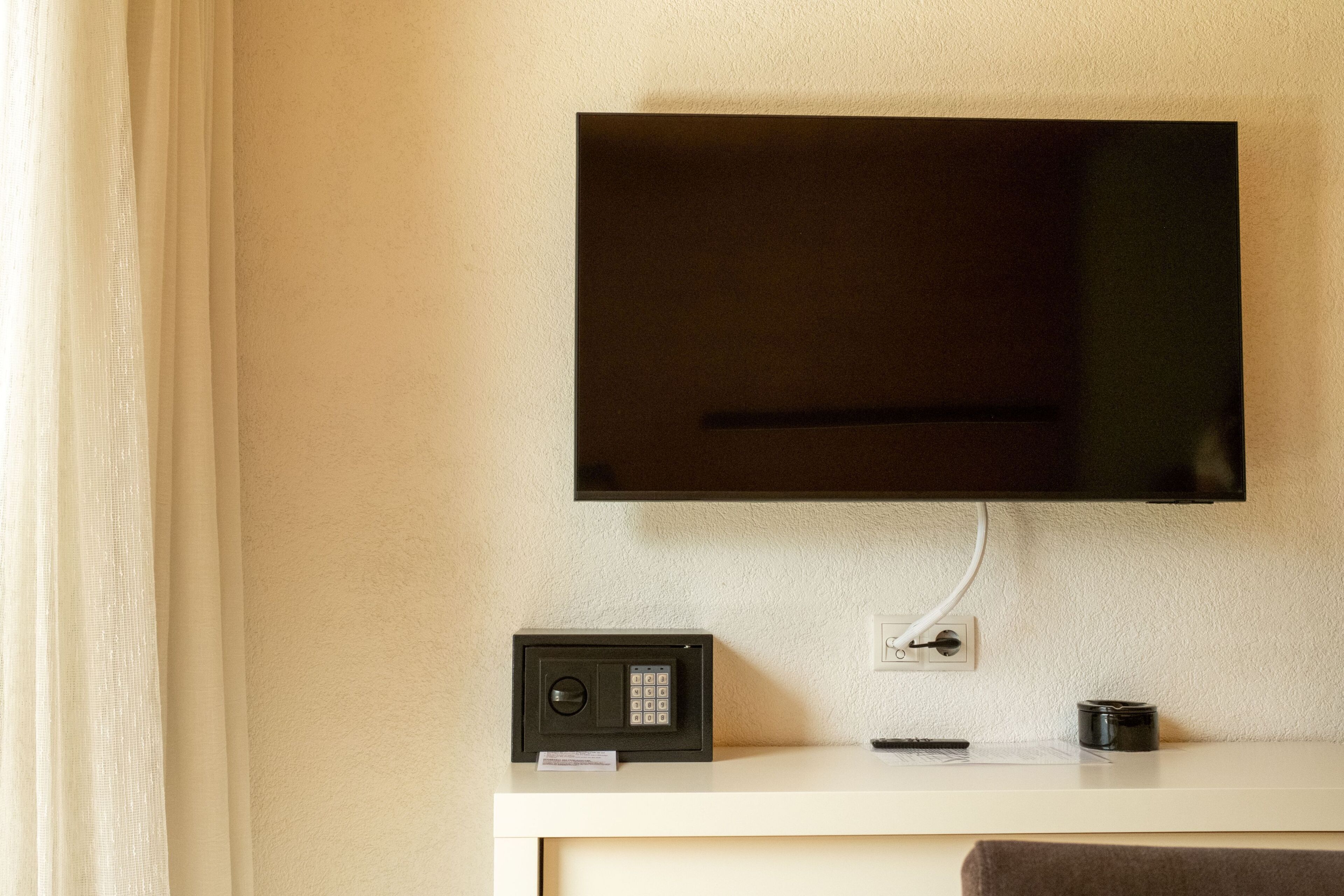 Un téléviseur à écran plat fixé au mur, au-dessus d’une console blanche, avec un appareil noir et une télécommande.