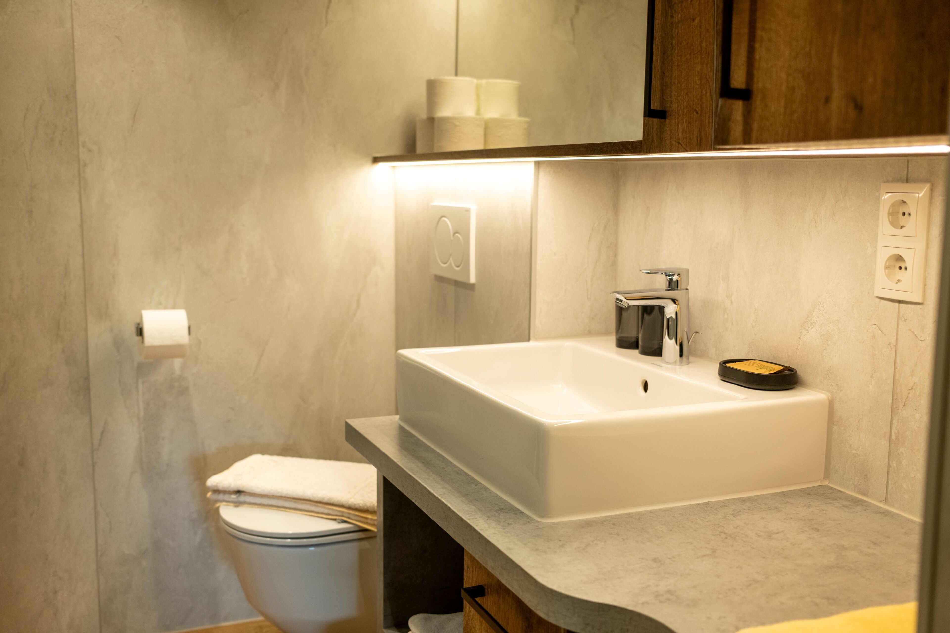 Un baño moderno con un lavamanos blanco, un inodoro y un espejo sobre el lavamanos.