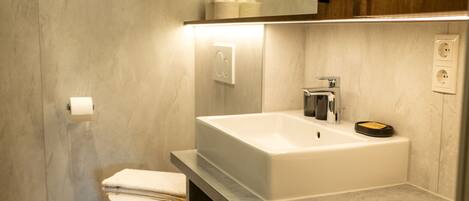 Un baño moderno con un lavamanos blanco, un inodoro y un espejo sobre el lavamanos.
