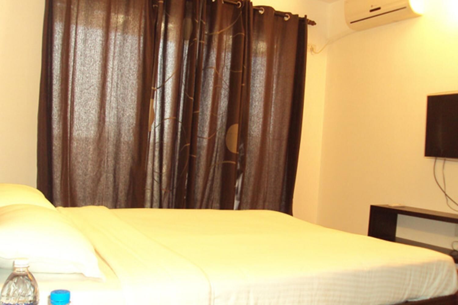 A room with a bed, a curtain, a wall-mounted TV, and a bottle on the side.