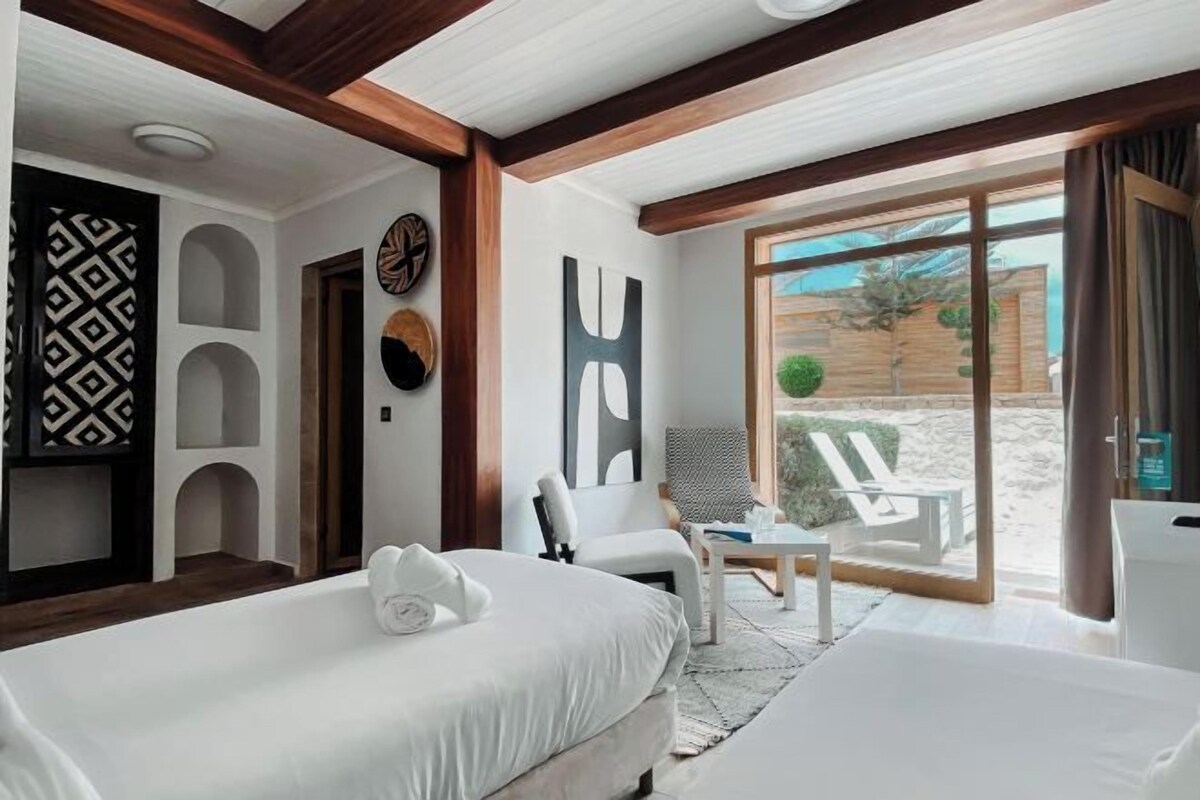 A hotel room with a bed, a chair, a small table, and a view of the outdoors.