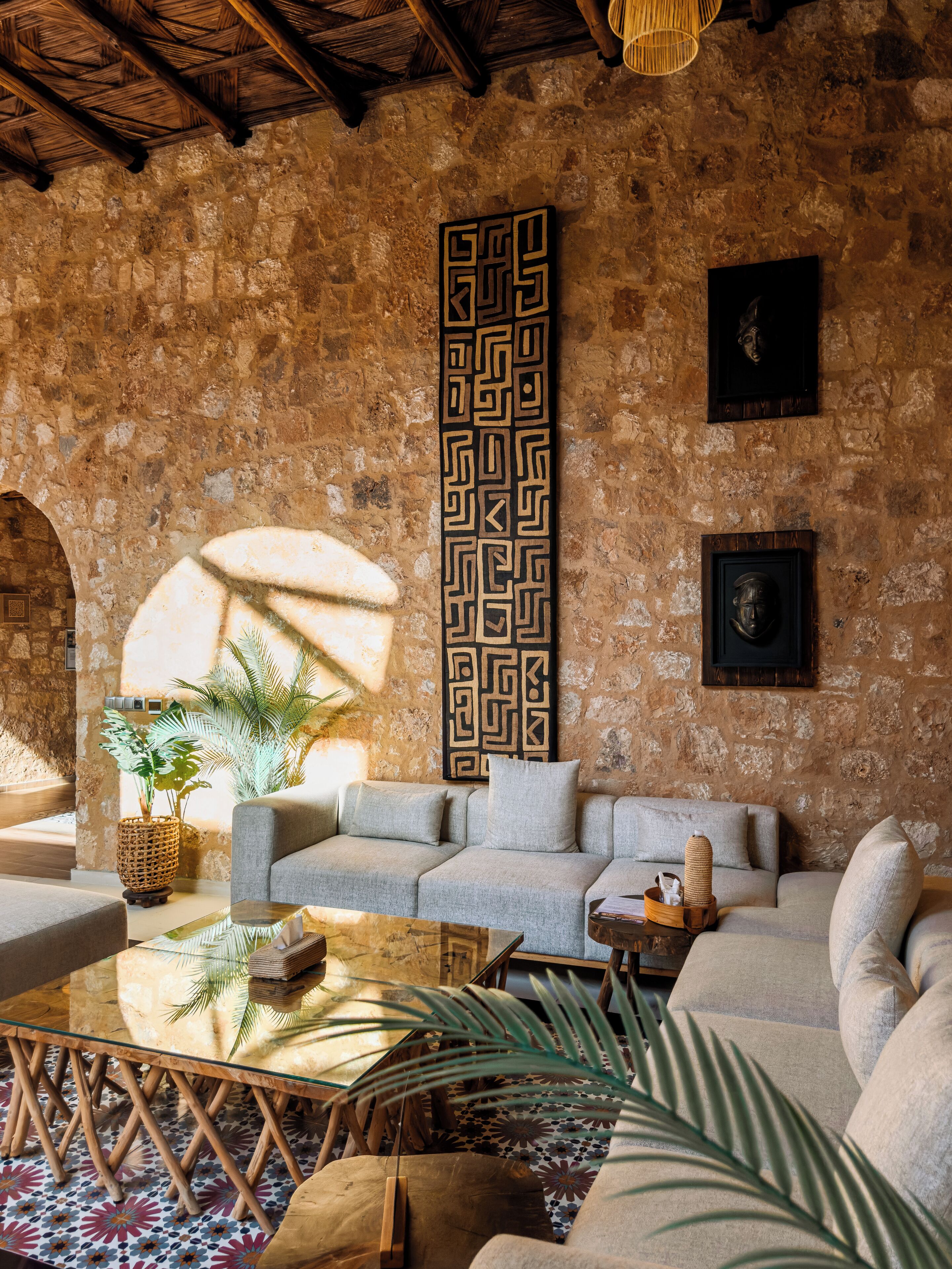A cozy living room with a stone wall, a patterned wall hanging, and a comfortable sofa set.