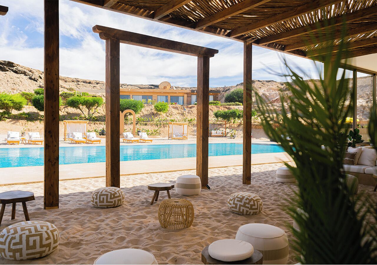 Un área junto a la piscina con pérgolas de madera, sillas de descanso y diferentes opciones de asientos.