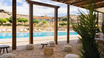 Un área junto a la piscina con pérgolas de madera, sillas de descanso y diferentes opciones de asientos.