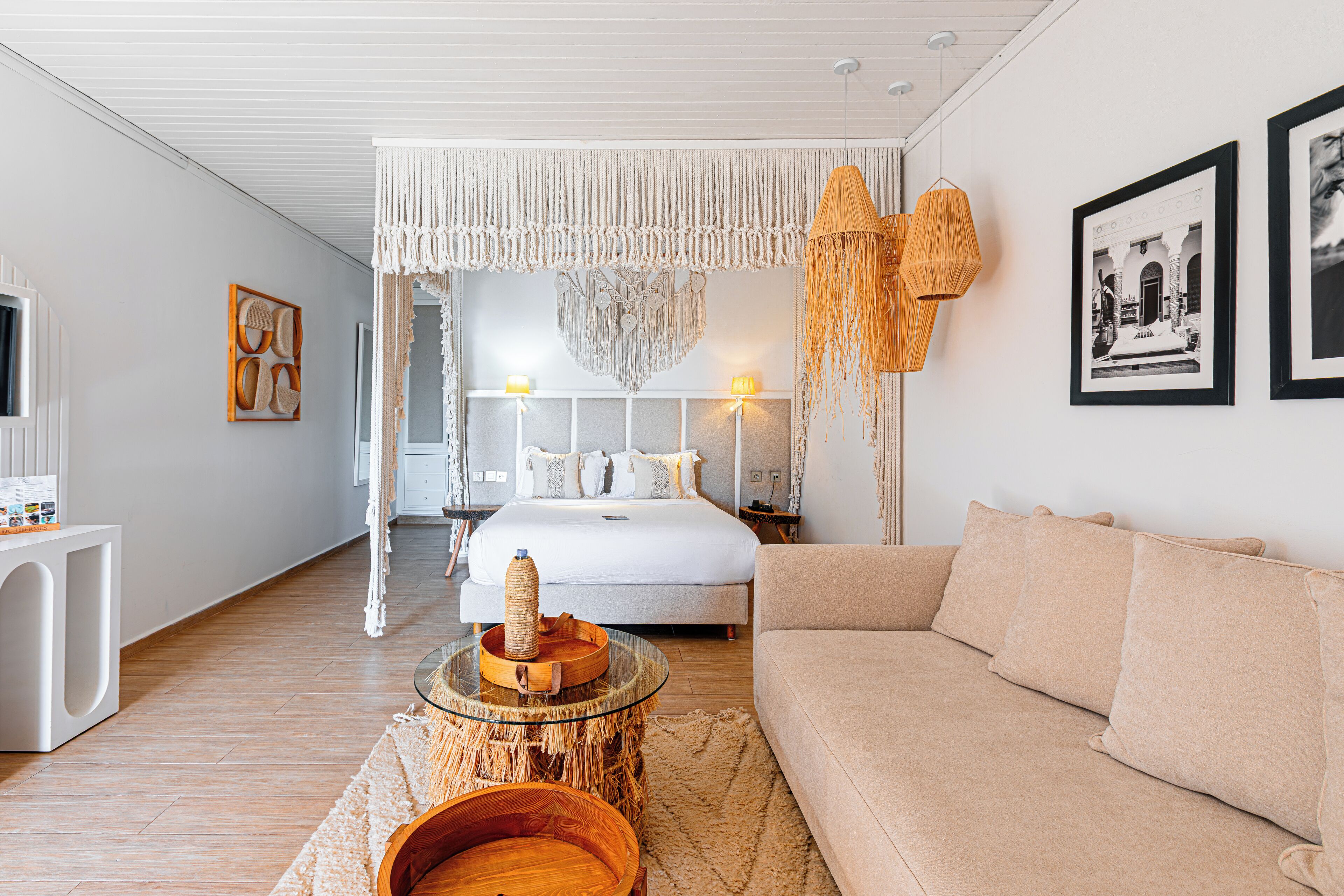 A modern bedroom with a large bed, bedside lamps, a glass coffee table, and a woven side table.