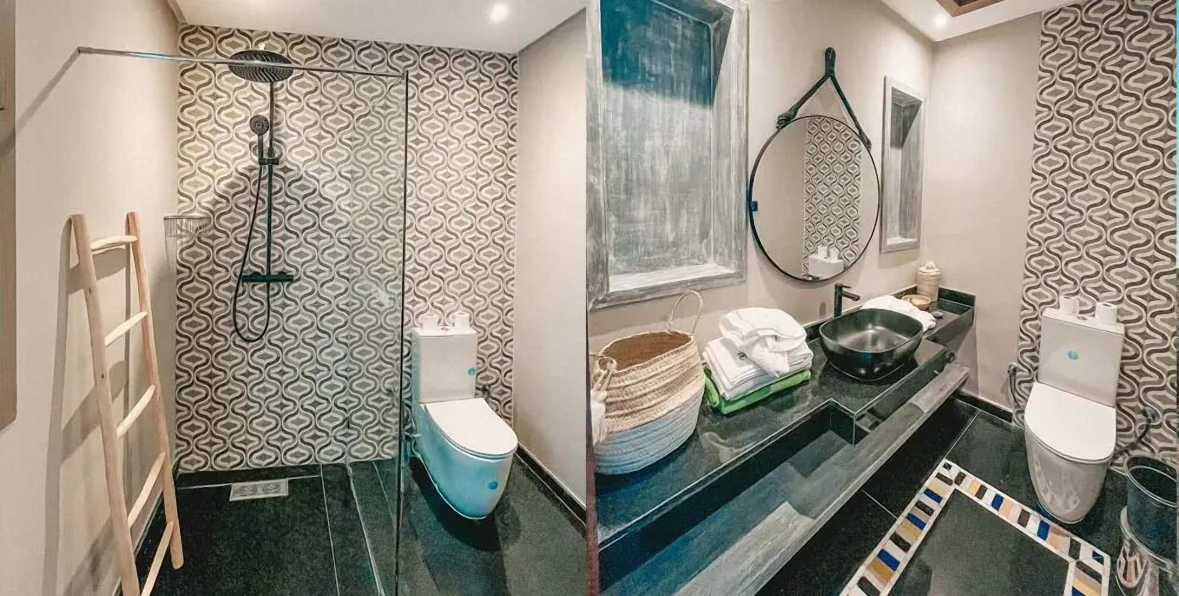 Un baño con papel tapiz estampado, cerramiento de ducha de vidrio, inodoro, lavamanos con espejo y una ventana pequeña.