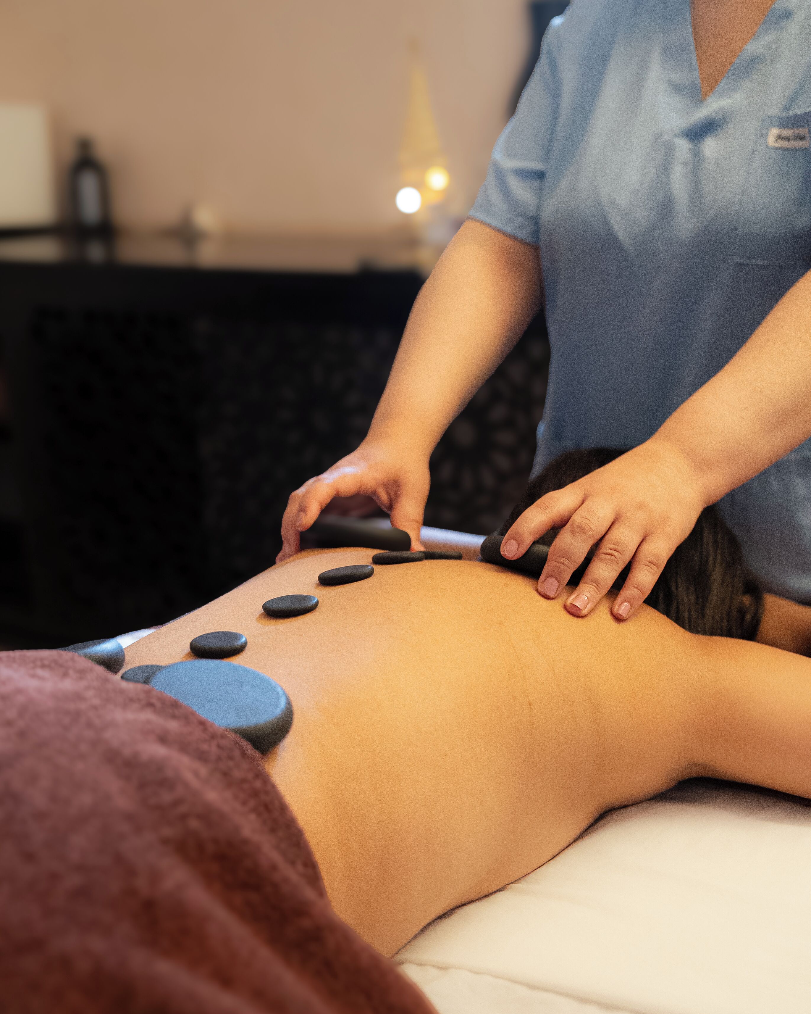 Une séance de massage où la personne est allongée sur le ventre sur une table de massage et reçoit des pressions exercées par les mains et des pierres chaudes utilisées par le thérapeute.