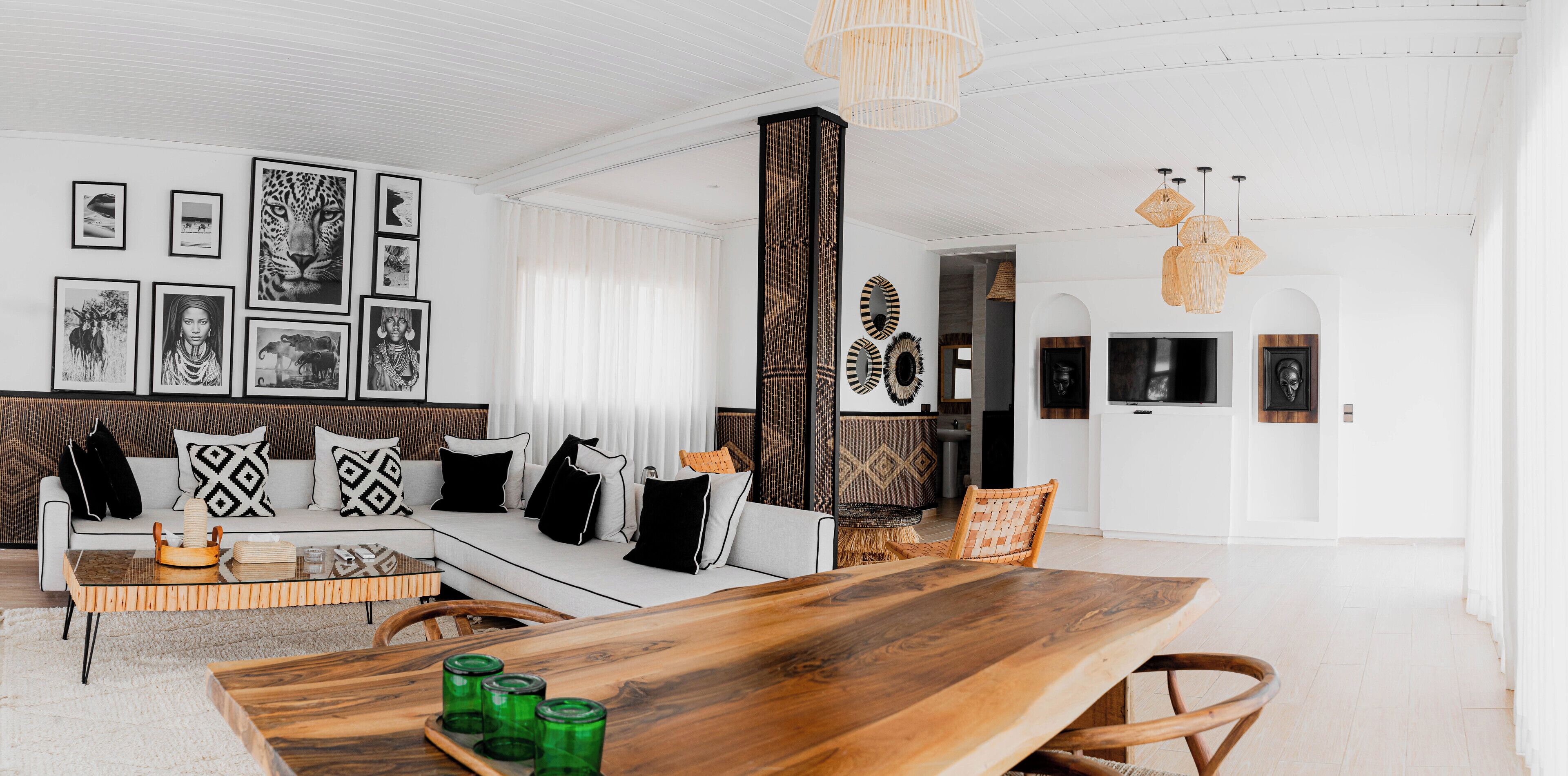 A modern living room with a wooden dining table, a sofa with patterned cushions, and a wall adorned with framed artwork.