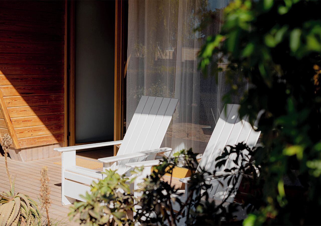 Une terrasse en bois avec deux chaises longues blanches et une petite table, donnant sur un jardin.
