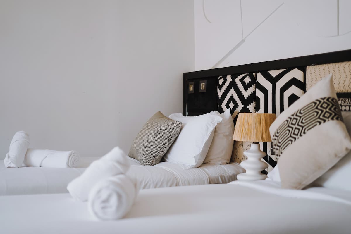 Una cama bien hecha con sábanas blancas, un cabecero estampado y una lámpara de noche.