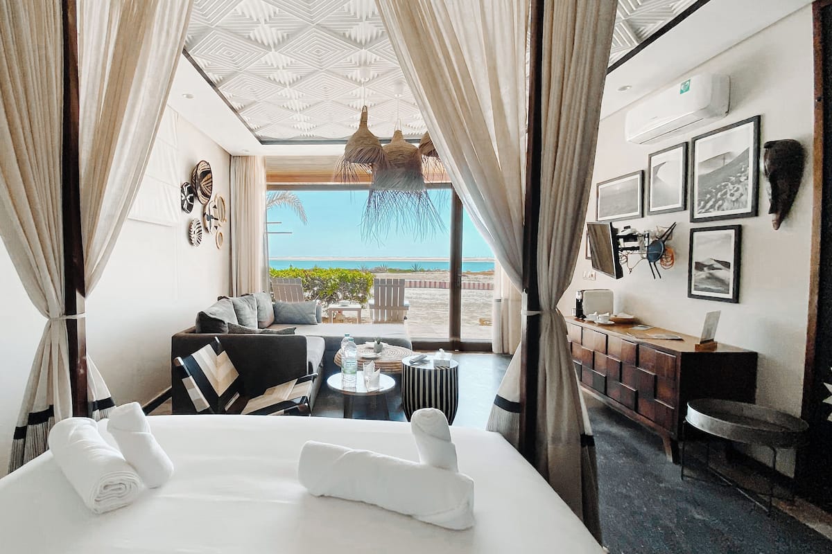 Una habitación de hotel con una cama, un pequeño rinc ón de estar con una mesa y vista a la playa.