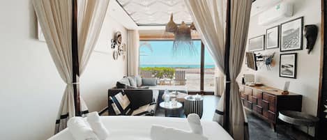 A hotel room with a bed, a small seating area with a table, and a view of the beach.