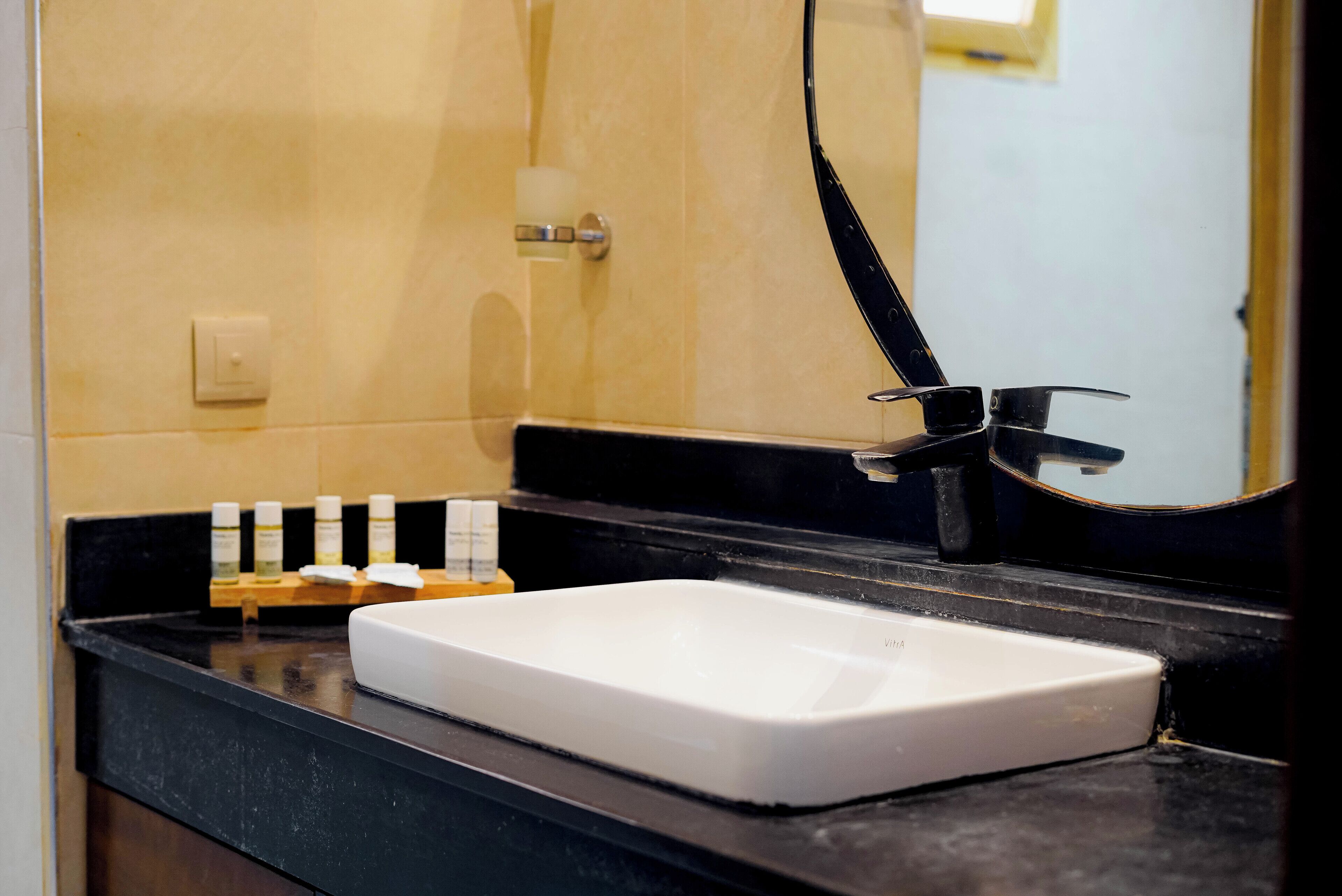 Une salle de bain avec un lavabo blanc, un plan de toilette noir et un miroir.