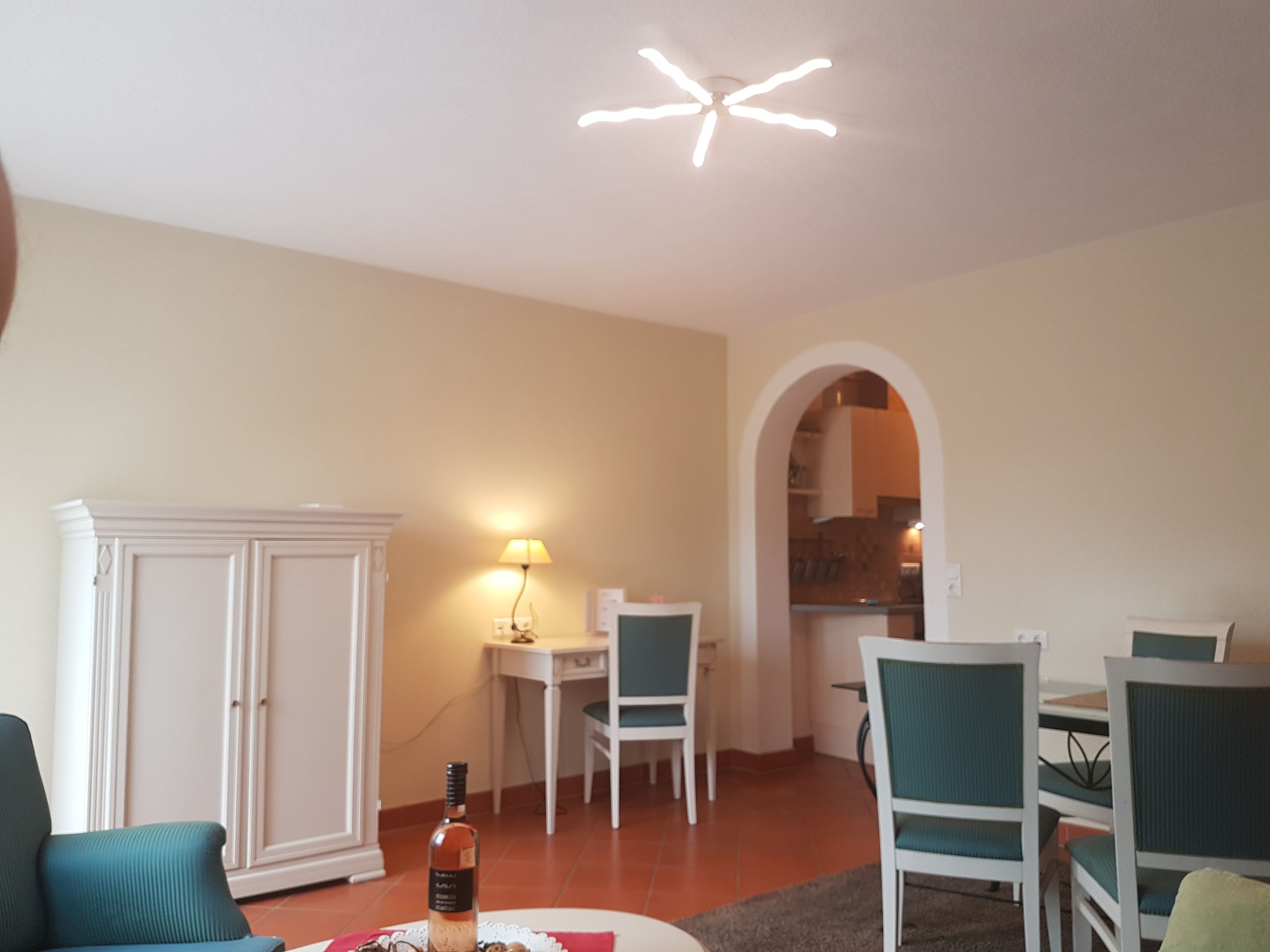 Una sala de estar con comedor, una cocina visible a través de un arco y una lámpara en el techo.