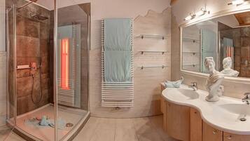 A modern bathroom with a glass-enclosed shower, a vanity with two sinks, and a large mirror with a sculpture.