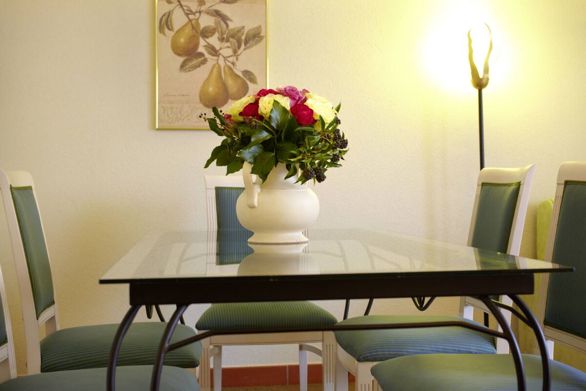 A dining table with a vase of flowers, surrounded by chairs with green cushions.
