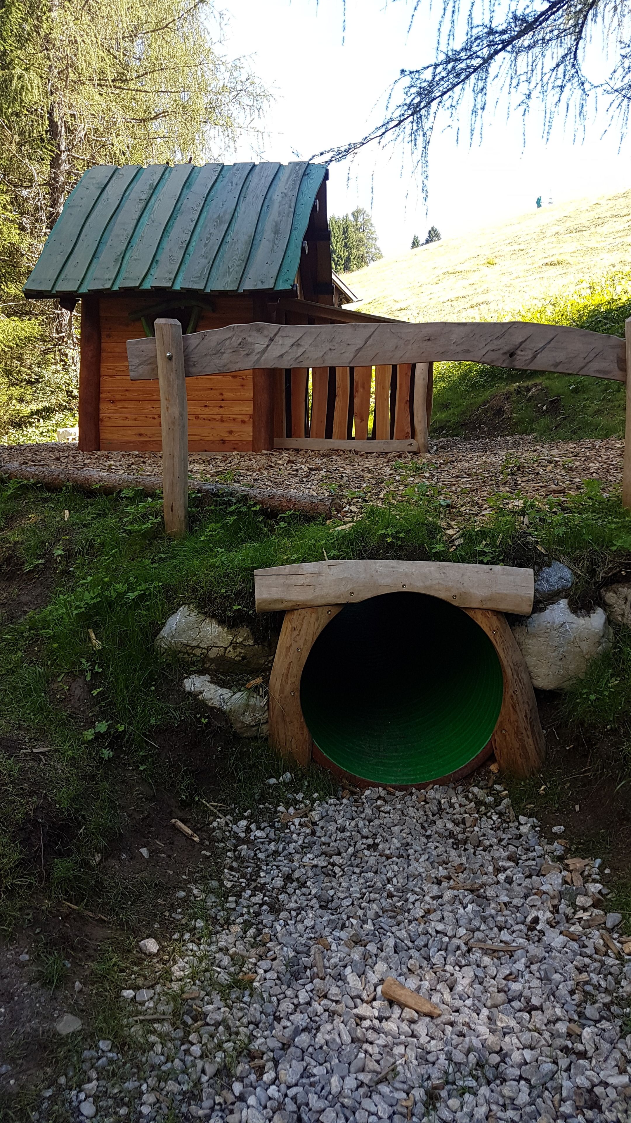 Puisesta leikkimökistä, jossa on vihreä katto ja tunnelin muotoinen sisäänkäynti.