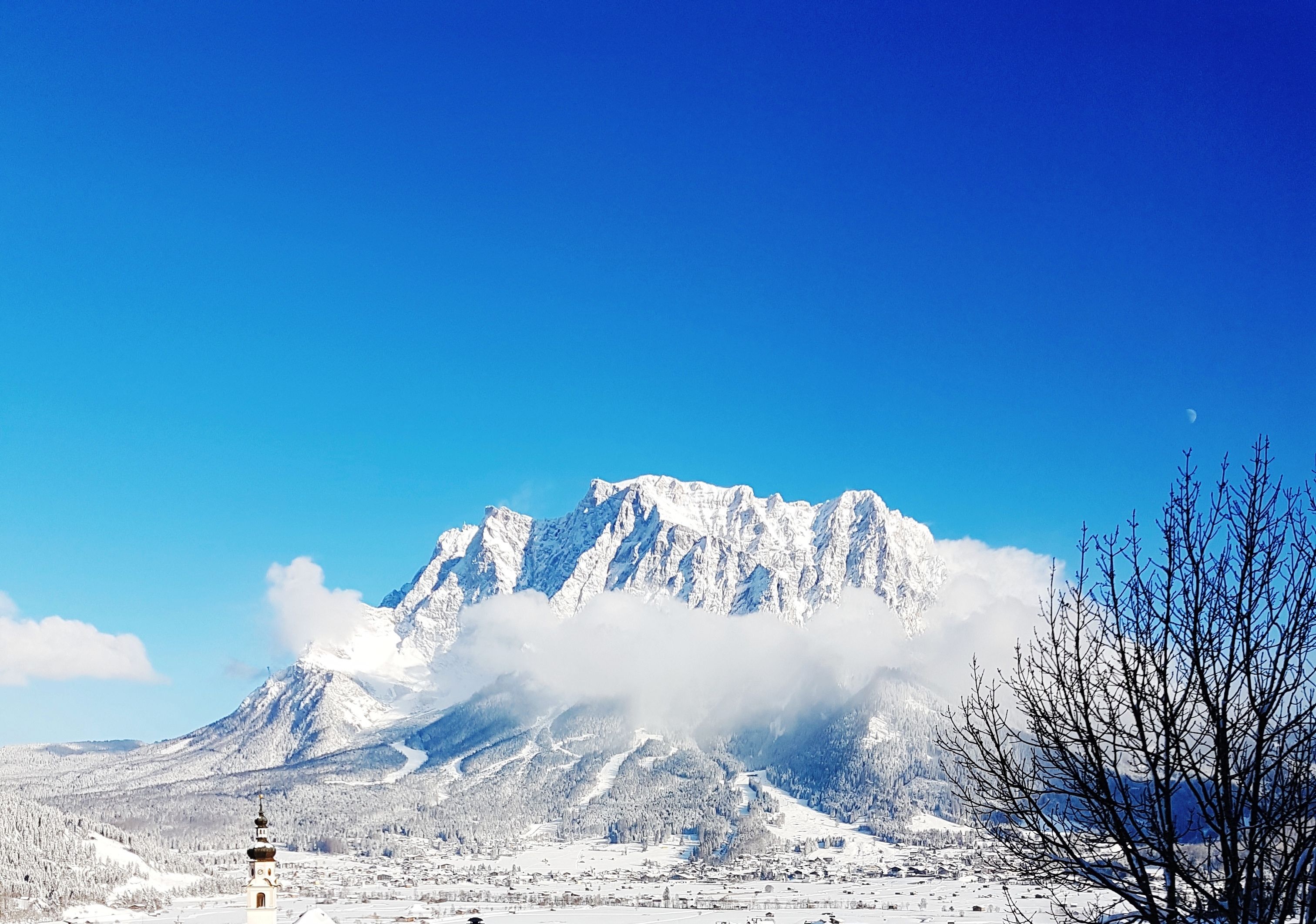 A snow-covered mountain with a clear sky and a small building with a tower in the foreground.