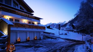 A hotel with a balcony, multiple garage doors, and a snow-covered landscape. - Landvilla Romantika (Lermoos)