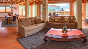 A spacious living area with a wooden ceiling, a sofa, a coffee table, and a dining area with chairs and a table. - Landvilla Romantika (Lermoos)