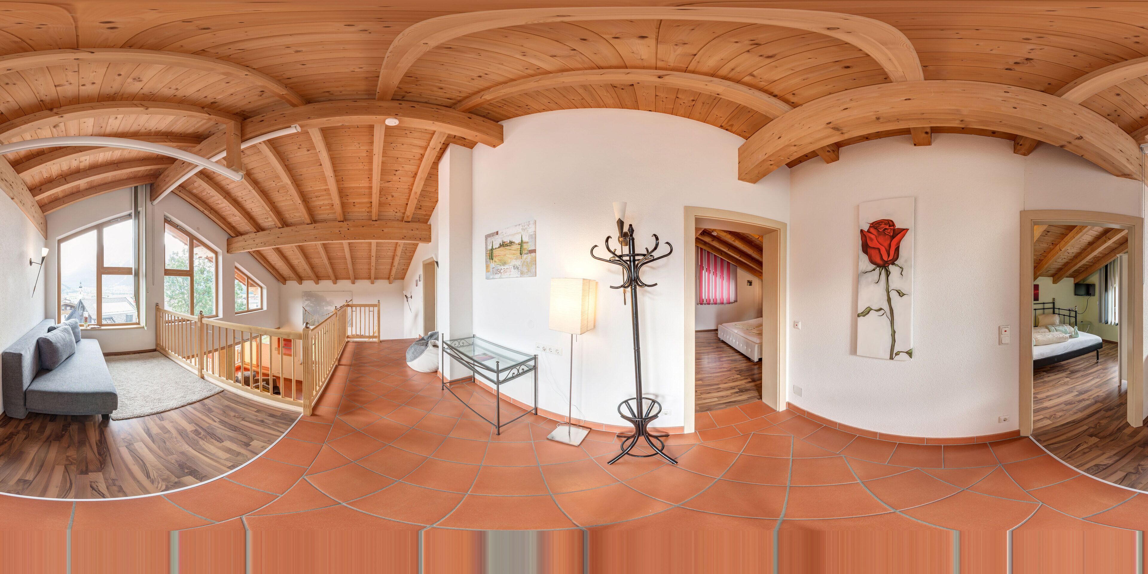 A spacious room with a high wooden ceiling, a sofa, a glass table, and a bed.
