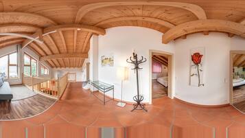 A spacious room with a high wooden ceiling, a sofa, a glass table, and a bed.