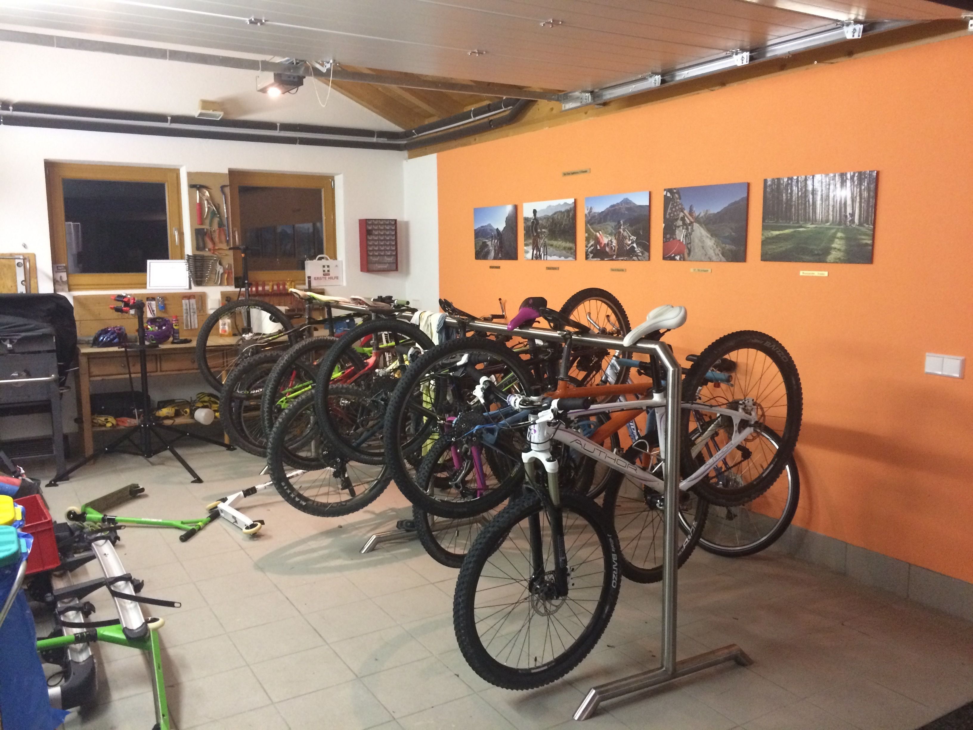 Una stanza con diverse biciclette appoggiate a una parete arancione, una scrivania in legno e una finestra con persiane.