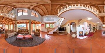 Un amplio salón con techo alto, vigas de madera, chimenea y televisor.