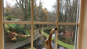 A window with a view of a river and trees, a wooden sculpture of a bird, and a stone wall. - Hewenden Mill Holiday Homes (Bradford)