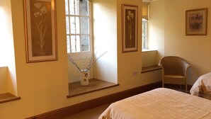 A bedroom with a large bed, a chair, and a window with a view of trees. - Hewenden Mill Holiday Homes (Bradford)