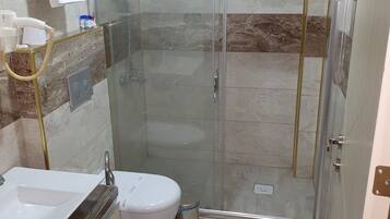 A modern bathroom with a glass-enclosed shower, a white sink, and a toilet.