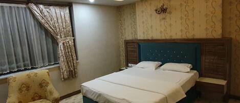 Un dormitorio con cama, una silla, una ventana con cortinas y una lámpara de pared.