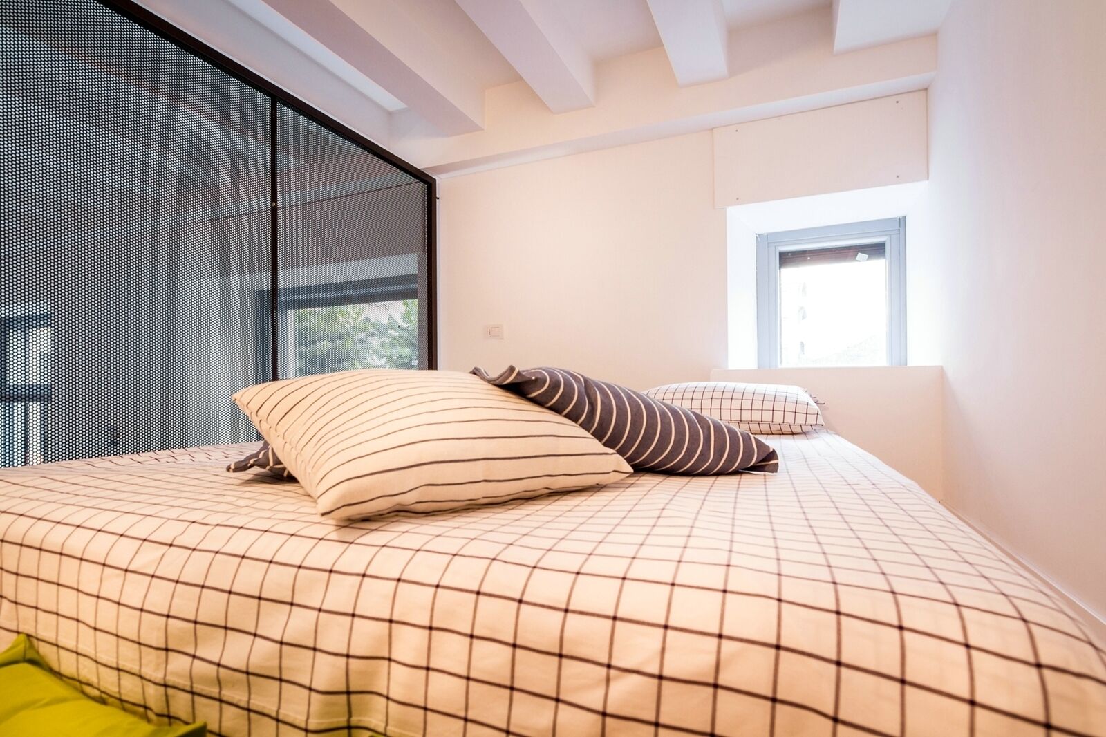 Una camera da letto con un letto, cuscini, una finestra e una zanzariera.
