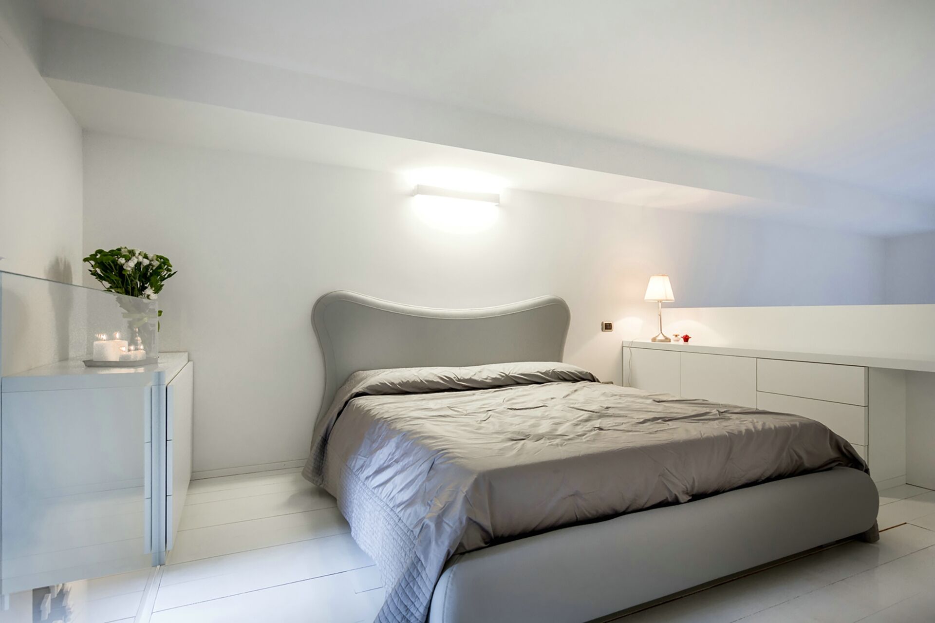 A modern bedroom with a bed, bedside table, and a nightstand with a lamp.